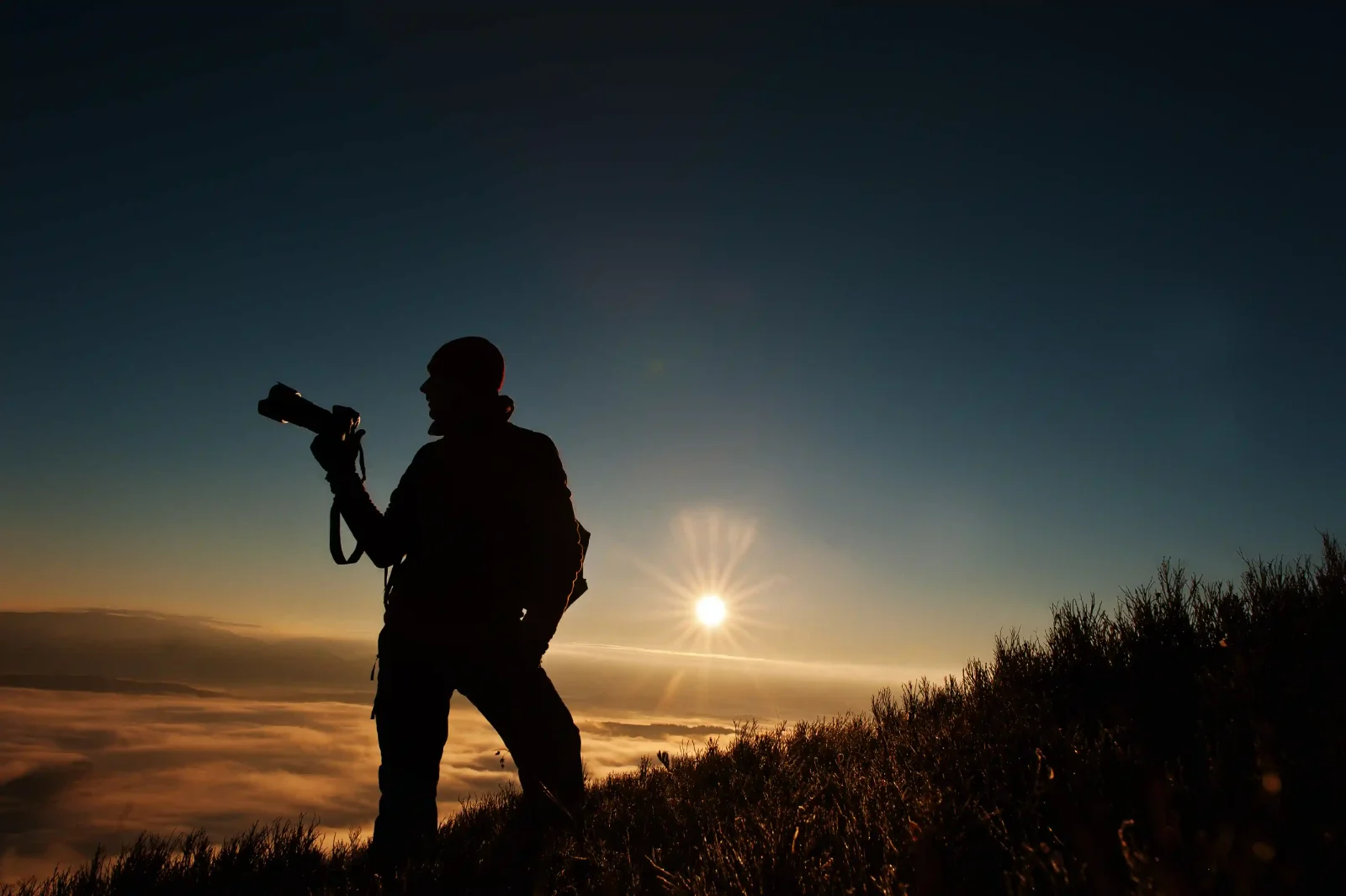 Photographer silhouette holding a camera against the setting sun, using photography composition techniques