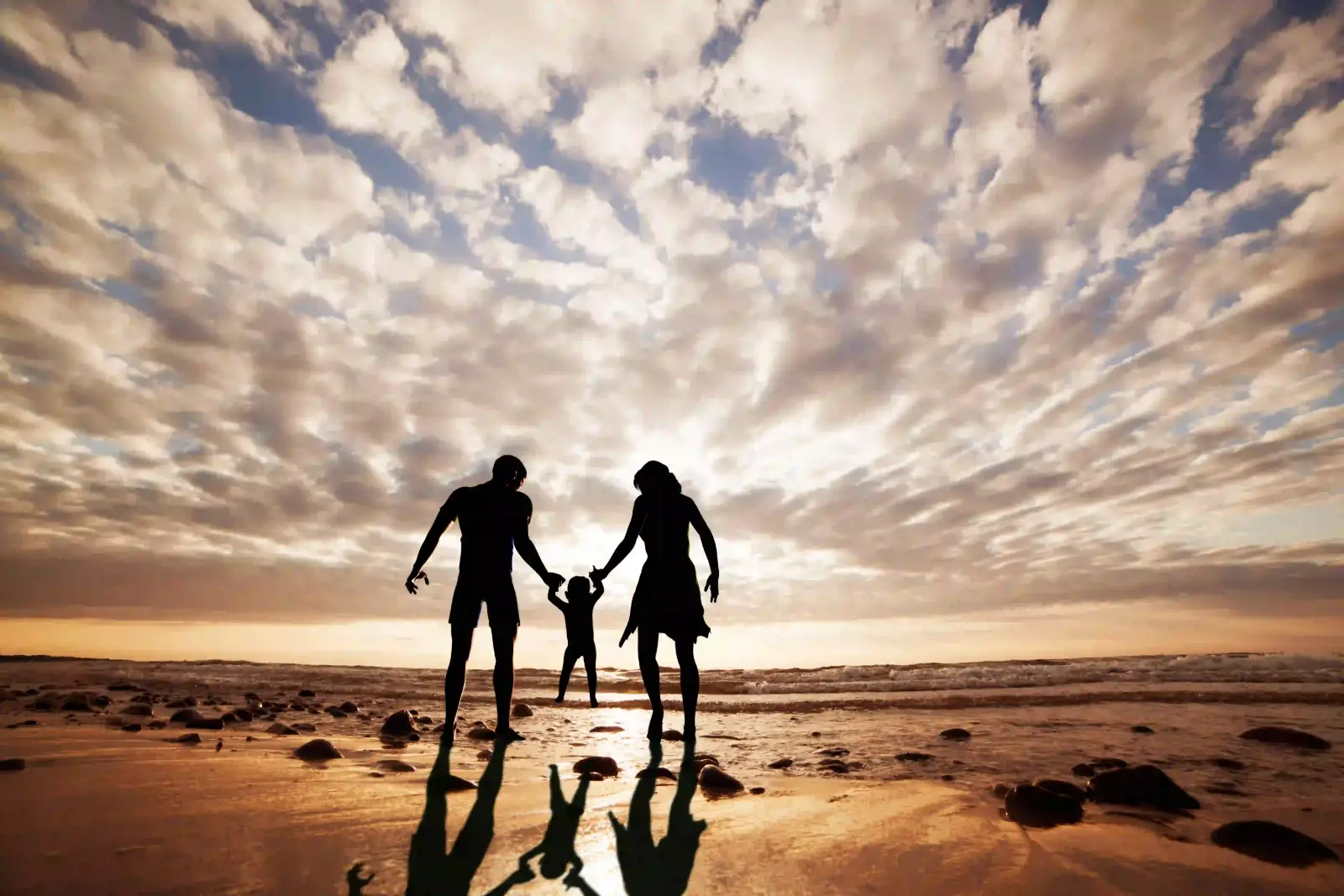 Silhouettes of a family on the beach against a bright evening sky
