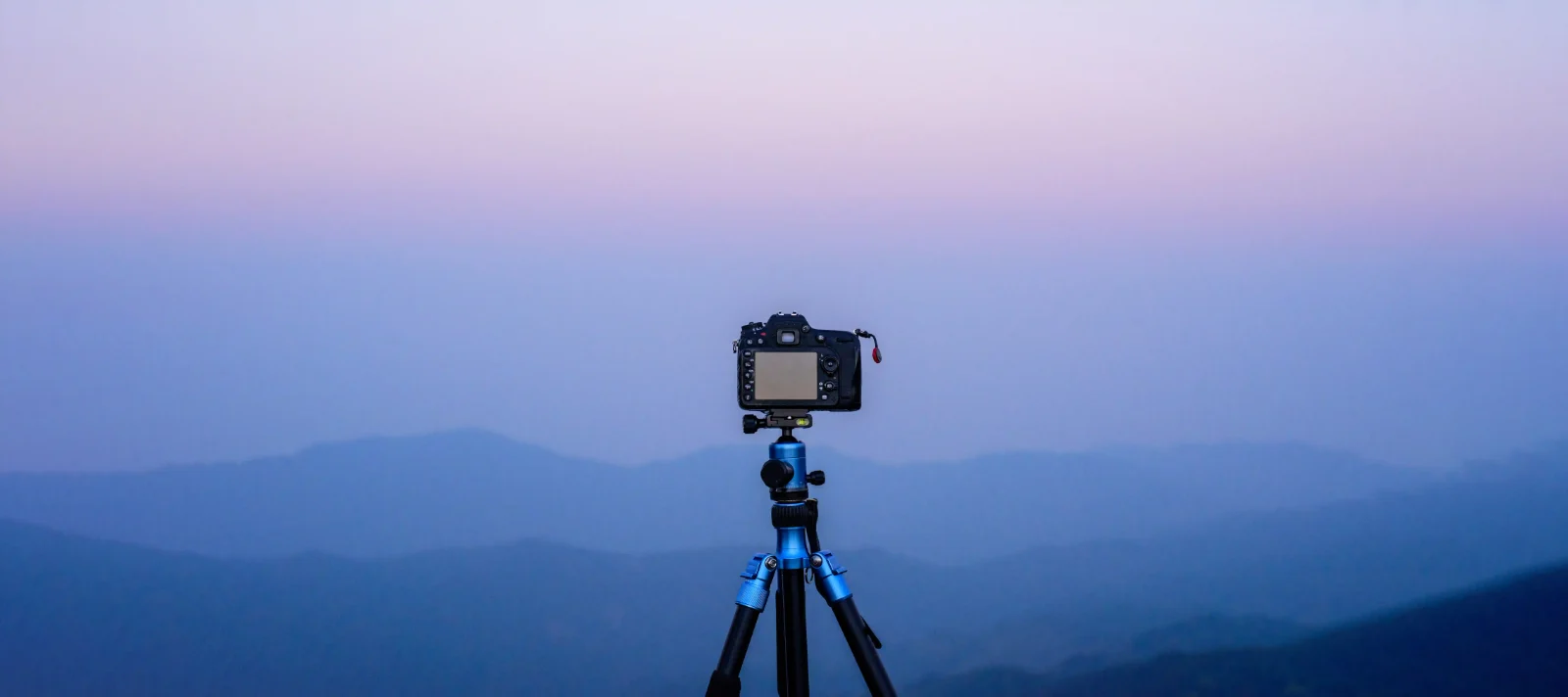 Camera on a tripod set up for landscape photography in the mountains